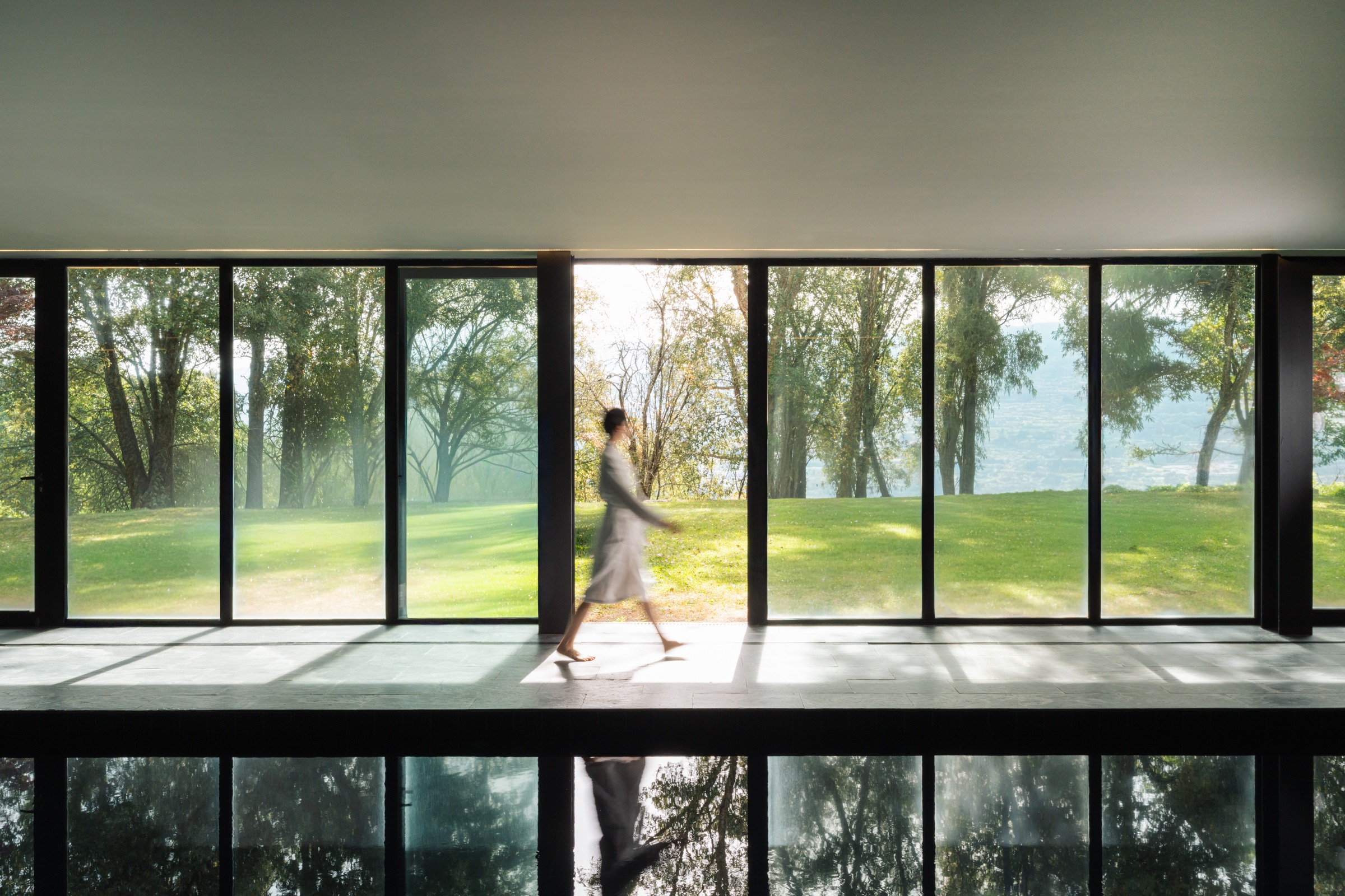 Guest walking beside an indoor pool overlooking a green landscape