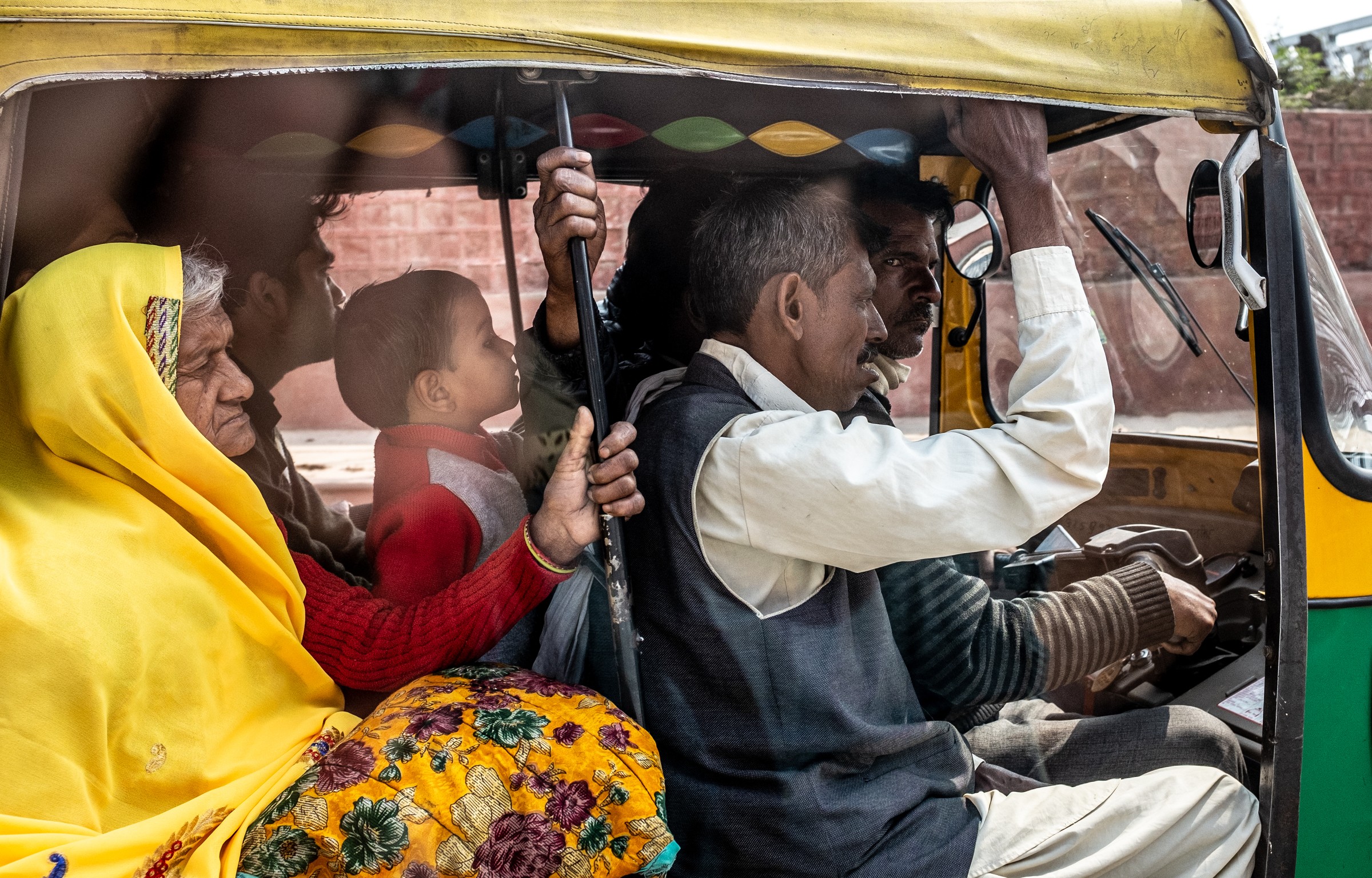 Passengers riding together in a yellow and green auto-rickshaw.
