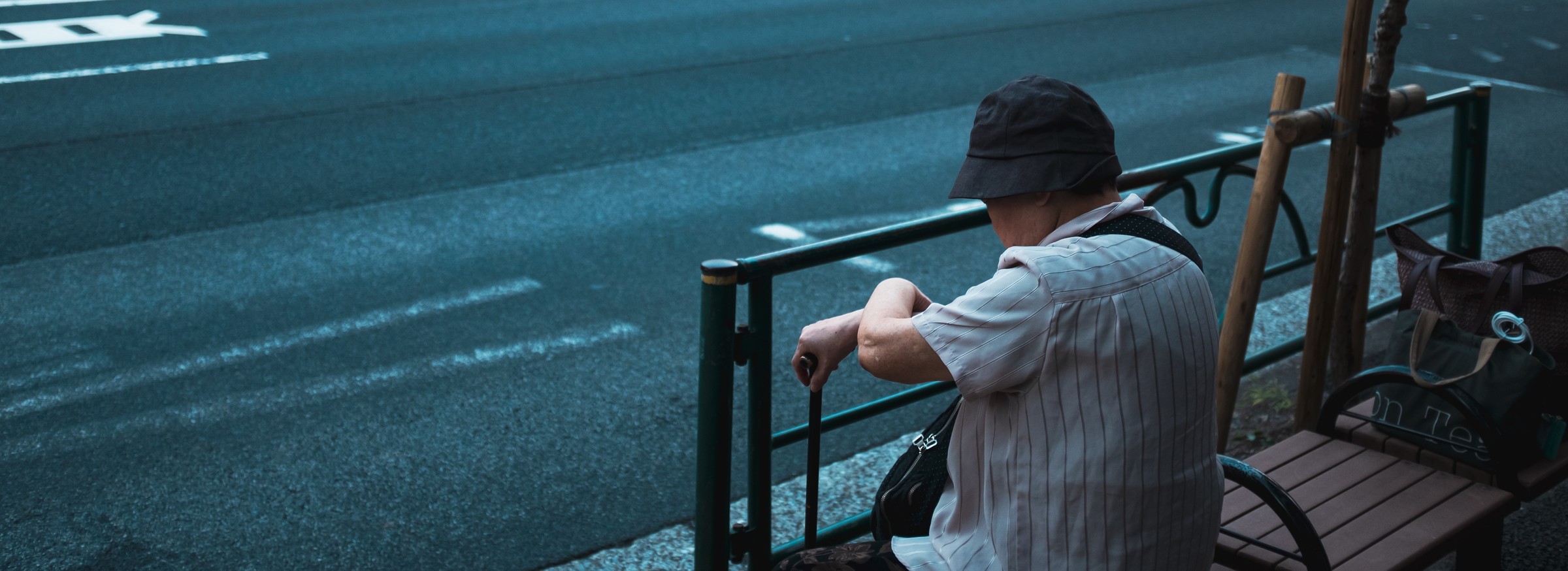 A person rests beside a railing overlooking a blue-toned street.