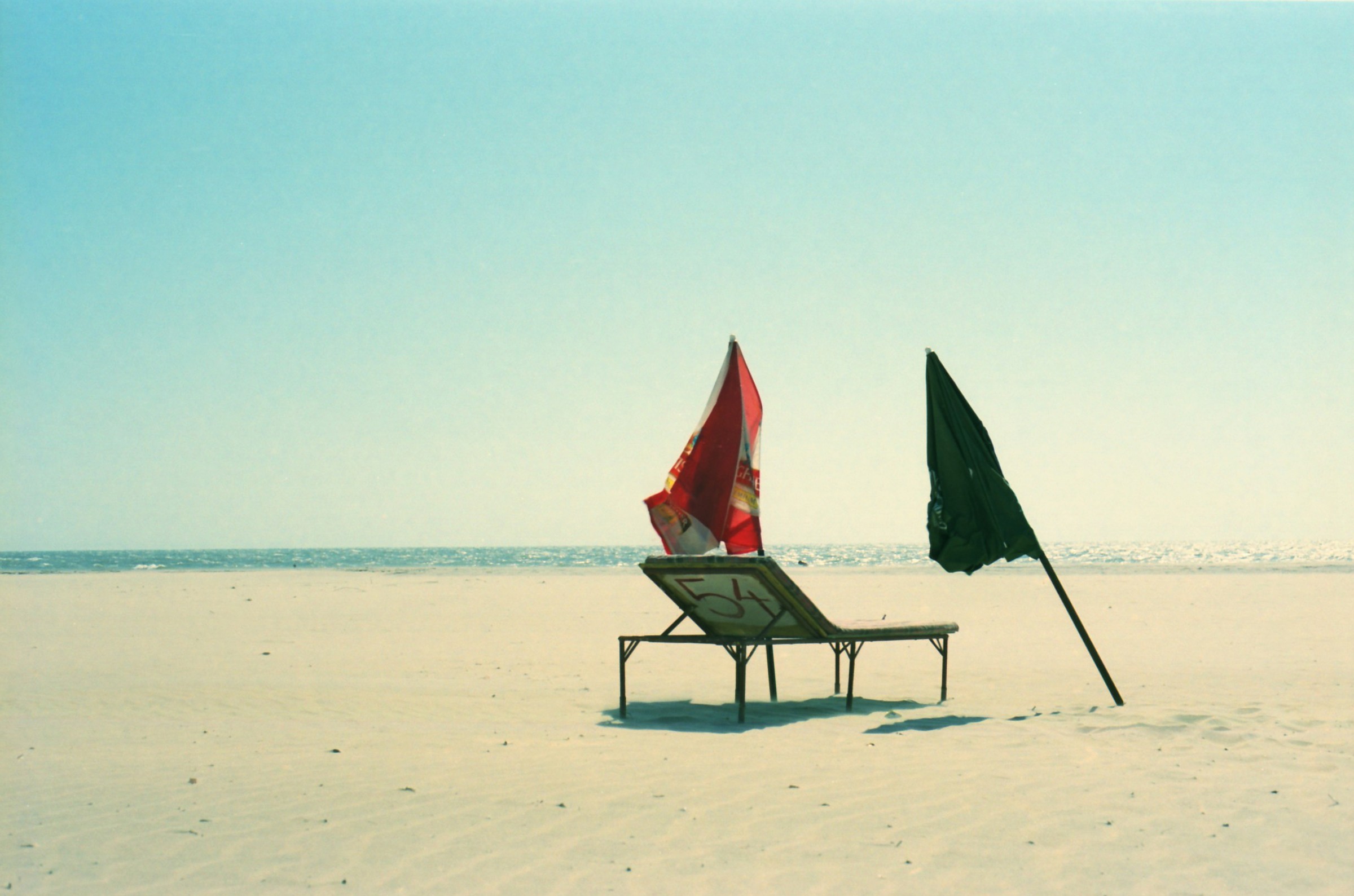 Two closed parasols and a lounger on an almost empty beach.