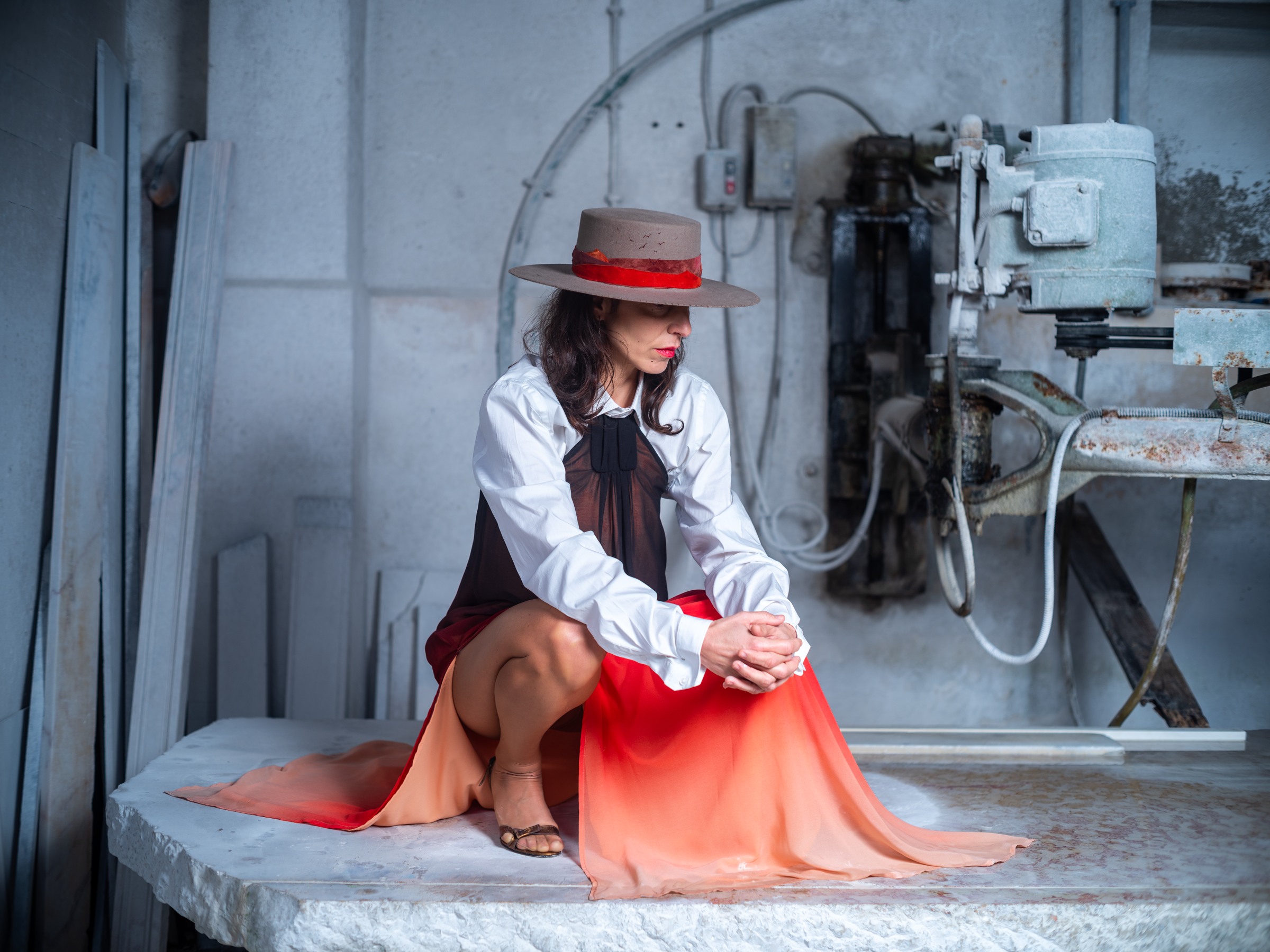 Seated woman in a hat and flowing red dress in an industrial space