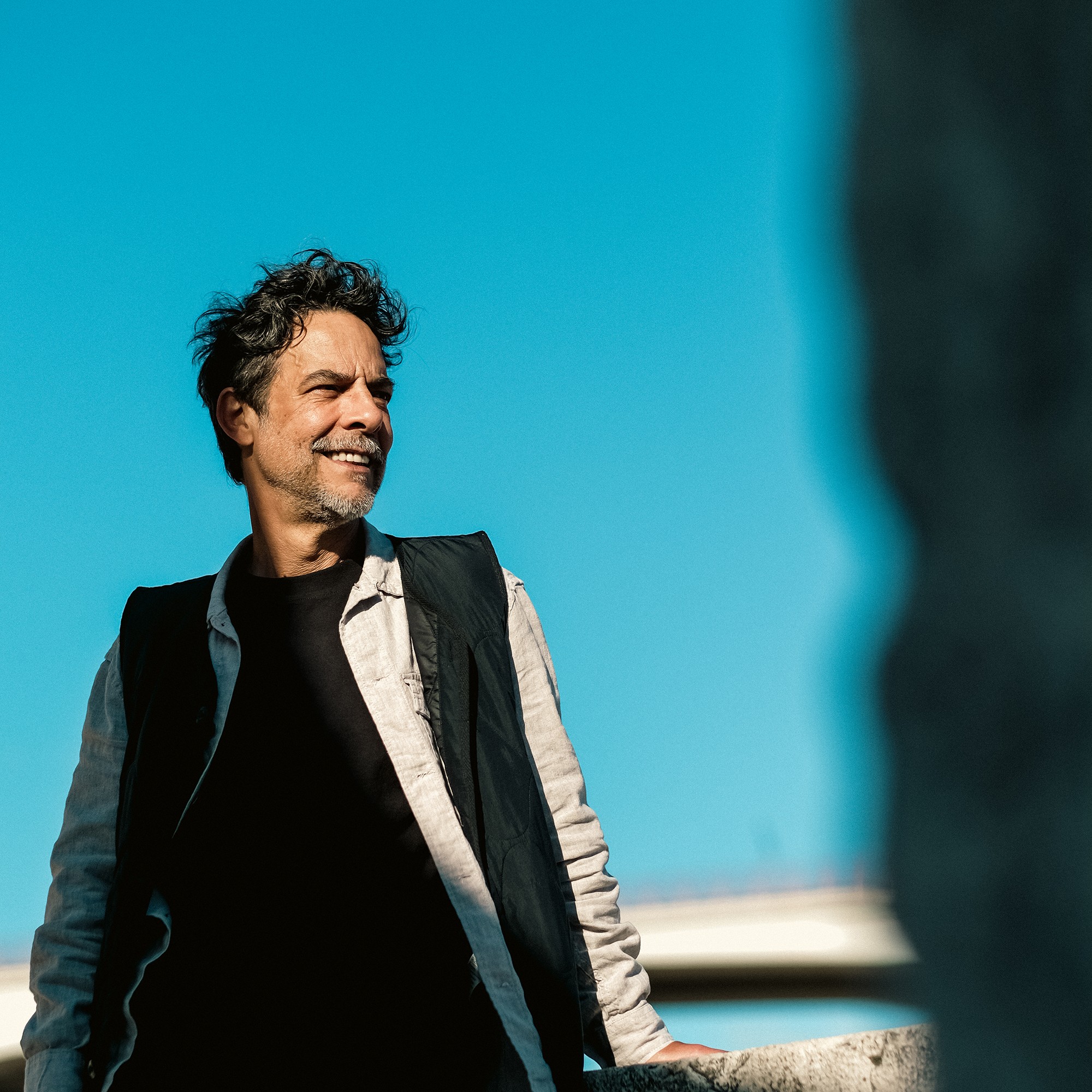 Portrait against a bright blue sky with a dark blurred foreground.